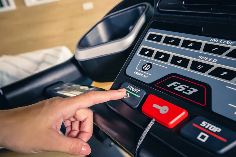 Close-up of hand pressing start button on SOLE treadmill control panel.