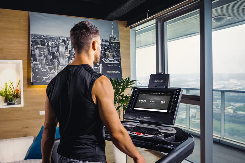 Man standing on SOLE F85 treadmill with city view in background, focused on screen displaying workout stats.