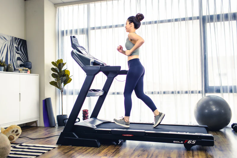 Woman runs on SOLE F65 treadmill in her home gym, focusing on cardio and muscle building.